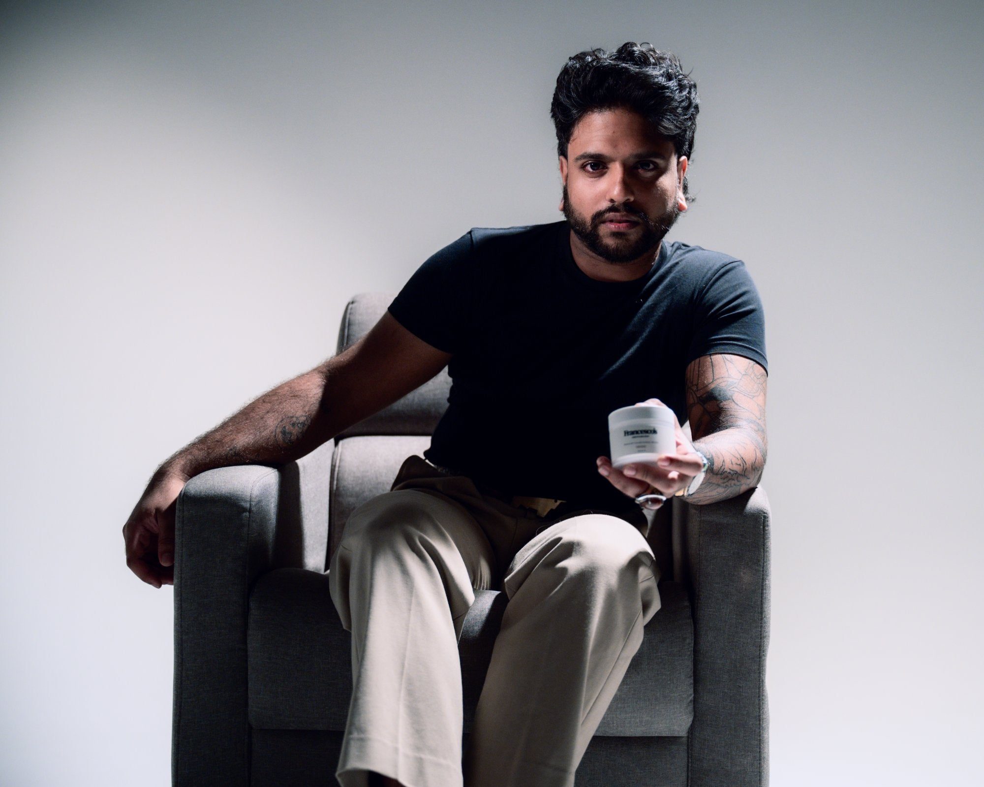 A man in a grey armchair holding a jar of Francesco's balm
